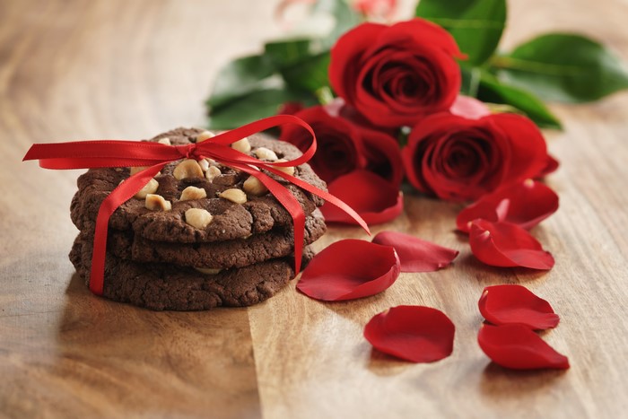 Chocolate cookies with hazelnuts tied with red ribbon and red roses