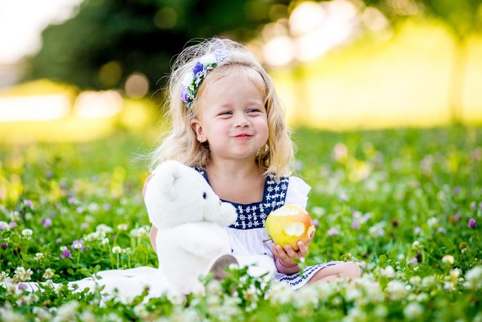 Little girl with teddy bear and apple in field