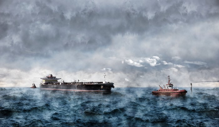 Tanker ship being towed by tugboat in rough seas