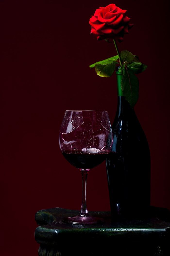 Broken wine glass with red rose and wine bottle
