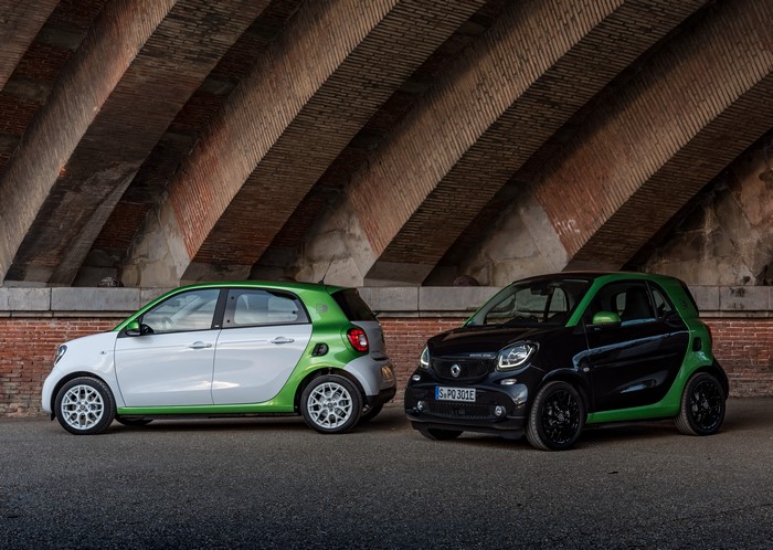 Two Smart electric drive cars under a brick archway