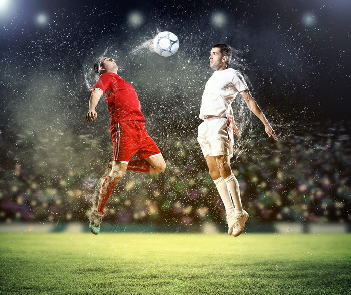 Two soccer players jumping to head the ball