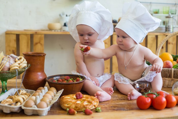 Two babies dressed as chefs with strawberries and baked goods