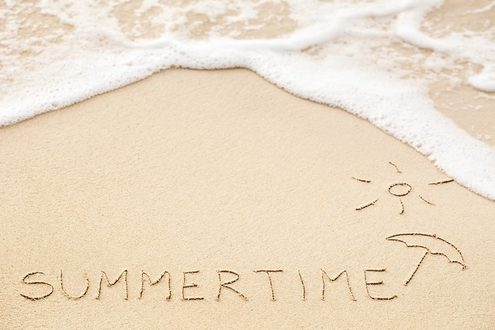 Summertime written in sand with sun and umbrella drawings