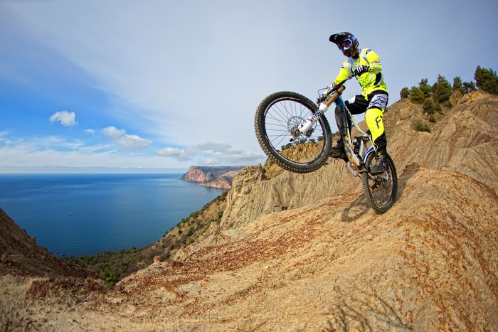 Man on bicycle performing a stunt on a cliff overlooking the sea