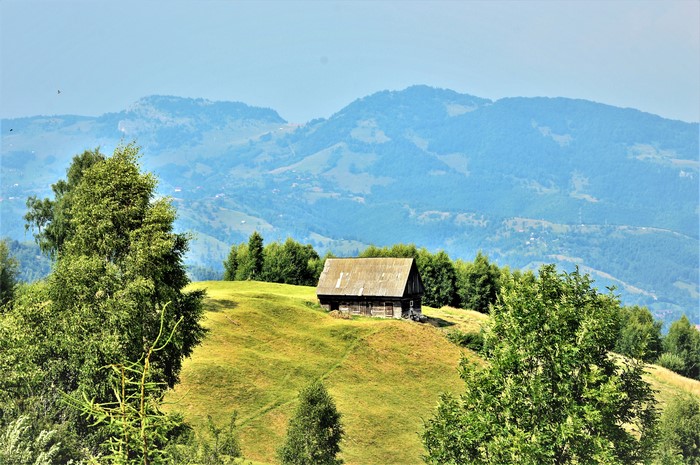 Wooden house on a grassy hill with mountains in the background