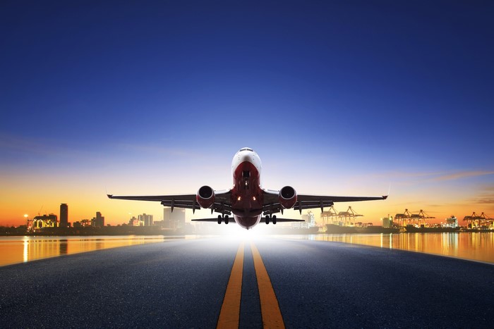 Airplane taking off at sunset over a city and harbor