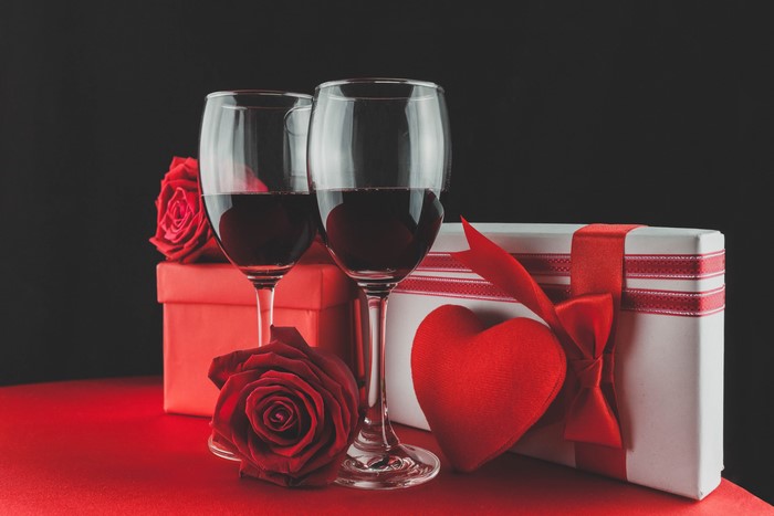 Two glasses of red wine with roses and gifts