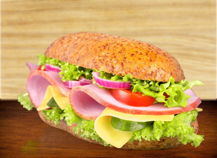 Ham and cheese sandwich with vegetables on a wooden table