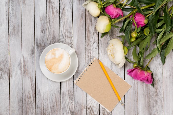 Cappuccino, peonies, and notepad on wood planks