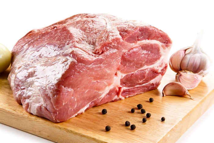 Raw pork shoulder with garlic and peppercorns on cutting board