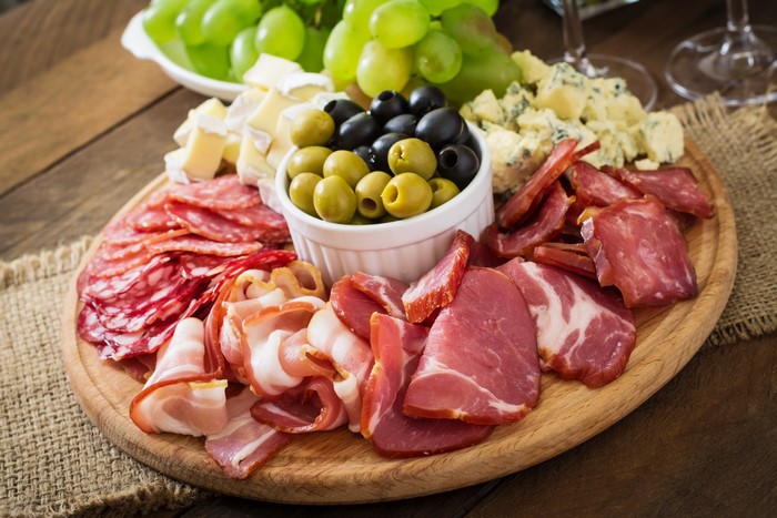 Charcuterie board with meats, cheeses, olives, and grapes
