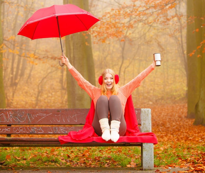 Woman with umbrella and thermos on a bench in autumn