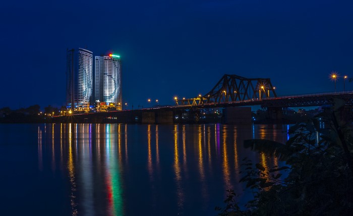 Long Bien Bridge and buildings over river at night in Ha Noi, Vietnam
