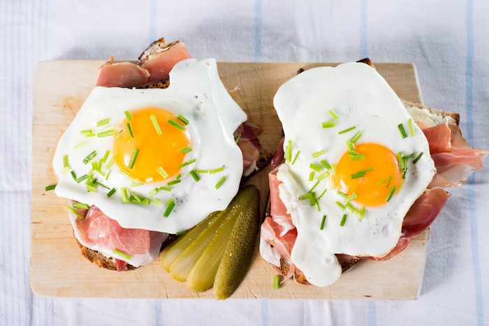 Two fried eggs with ham and pickles on bread