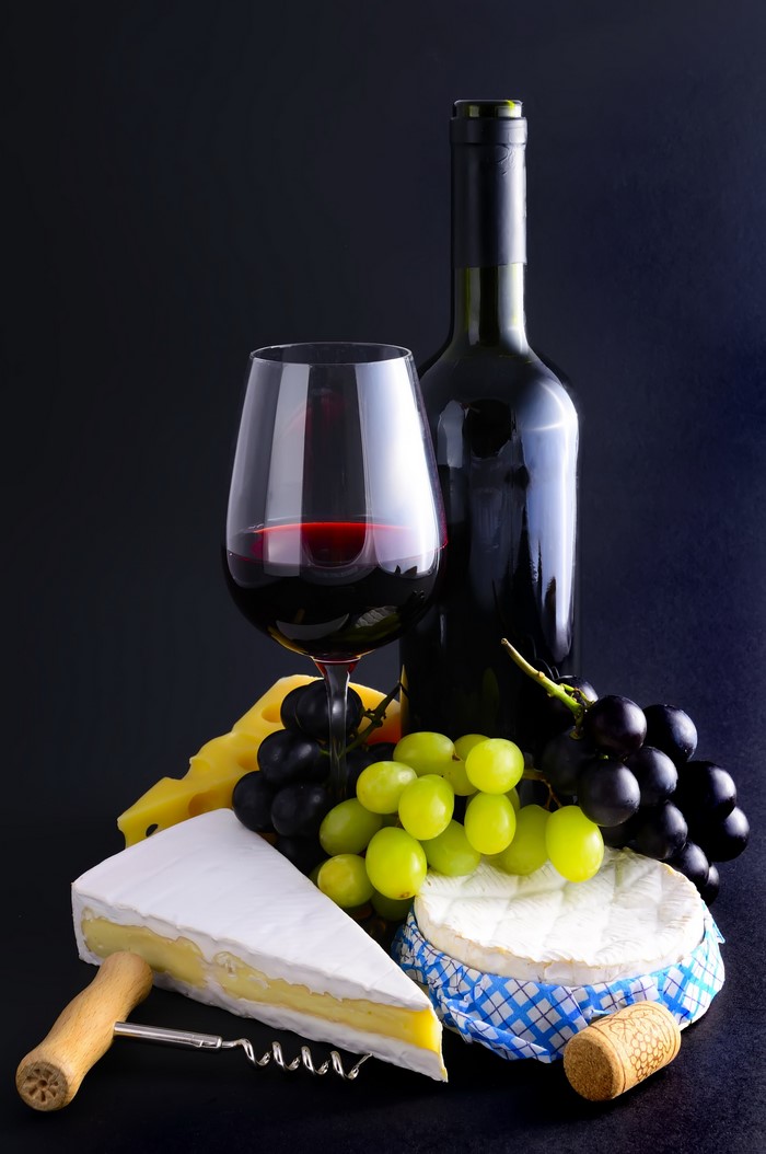 Wine bottle, glass, grapes, and cheese on black background