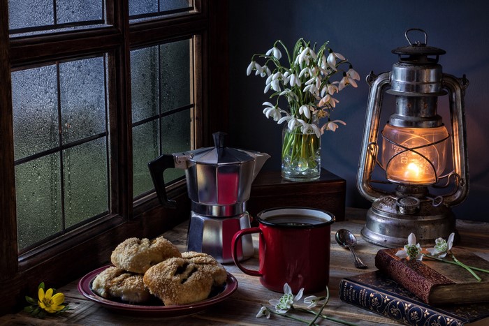 Still-life with kerosene lamp, snowdrops, coffee, and pastries