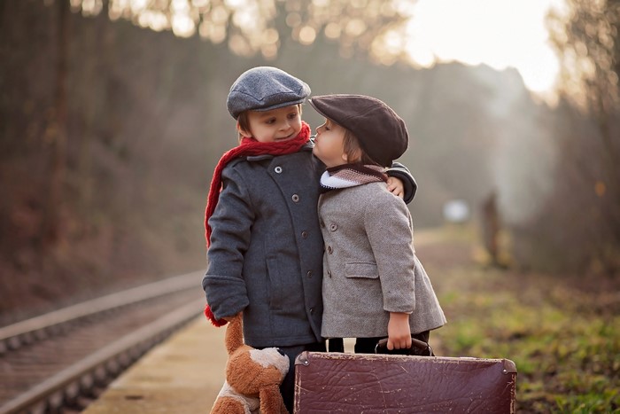 Two boys with suitcase and teddy bear on train platform