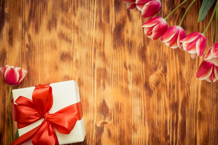 Gift box with red bow and tulips on wooden background