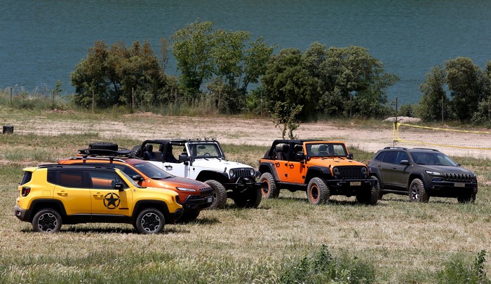 Four Jeeps parked on grassy terrain near a body of water