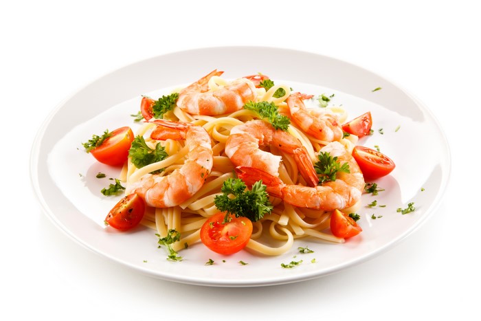 Shrimp pasta with tomatoes and parsley on a white plate