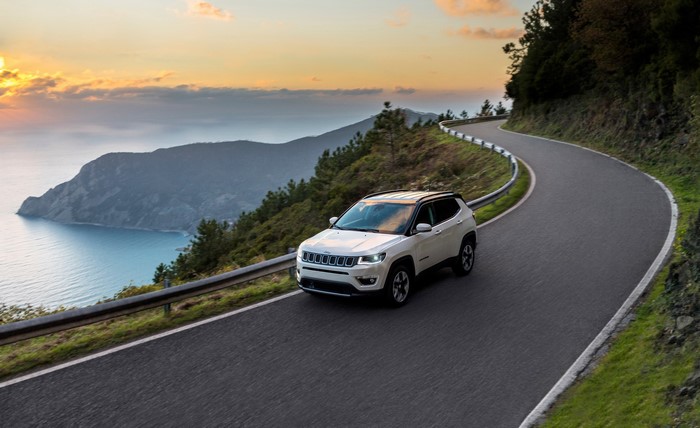 White Jeep Compass driving on a winding road by the sea