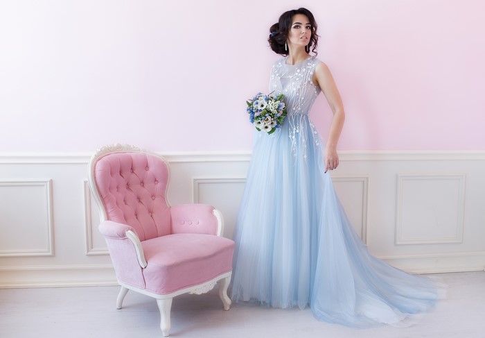 Woman in blue dress holding bouquet near pink armchair