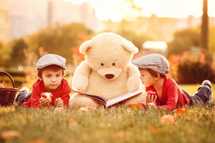 Two boys and a teddy bear reading a book