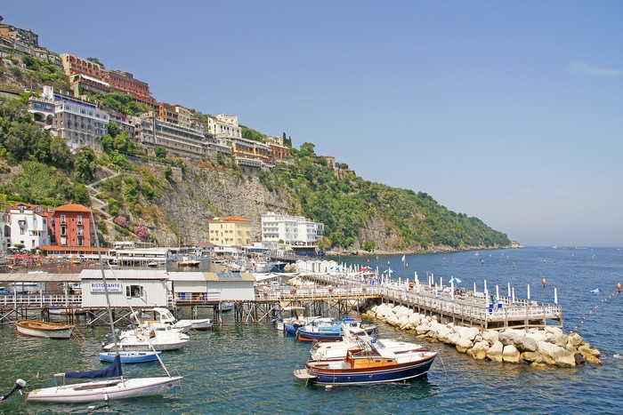 Boats docked in a marina below cliffside buildings in Sorrento, Italy