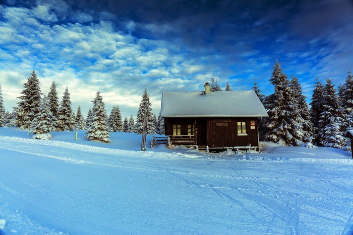 Winter cabin in snowy forest with dramatic sky