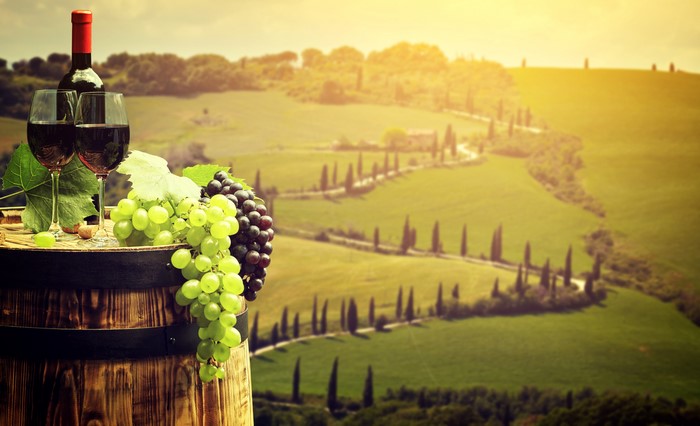 Wine bottle, glasses, grapes on barrel in Tuscany