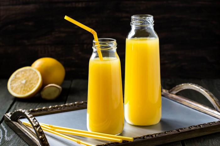Two bottles of orange juice with oranges and ginger