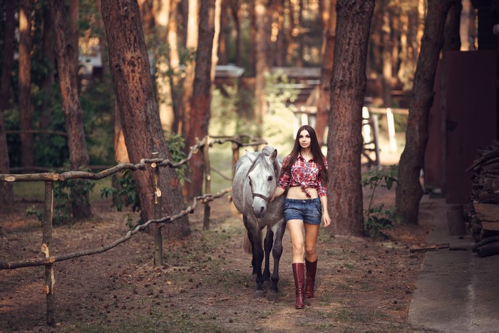Woman in plaid shirt and shorts walking a horse