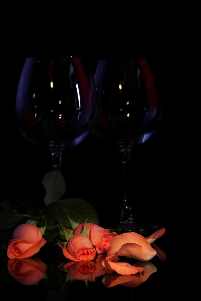 Two wine glasses and pink roses on a black background