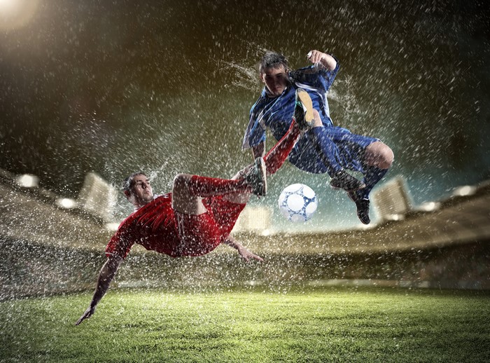 Two soccer players in mid-air during a match with water splashes