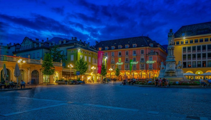 Town square with monument and buildings in Bolzano, Italy at dusk