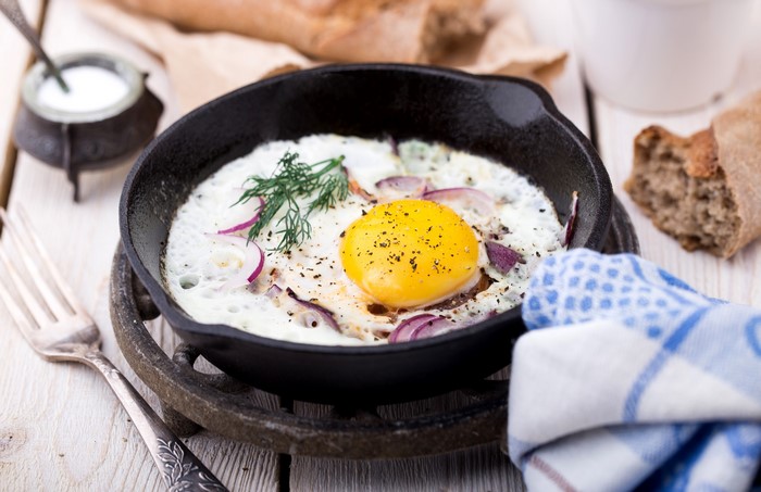 Fried egg with red onion and dill in a cast iron pan