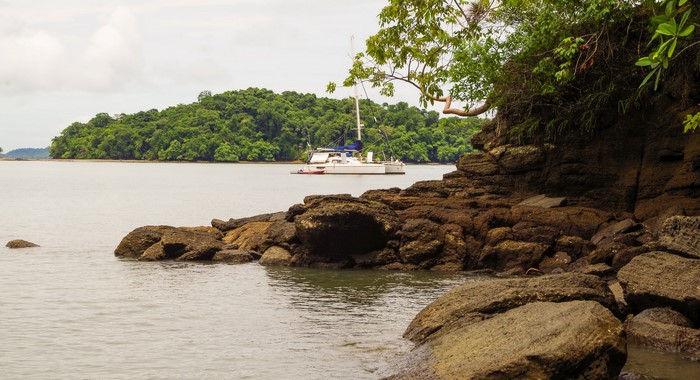 Catamaran anchored near rocky shore and lush island