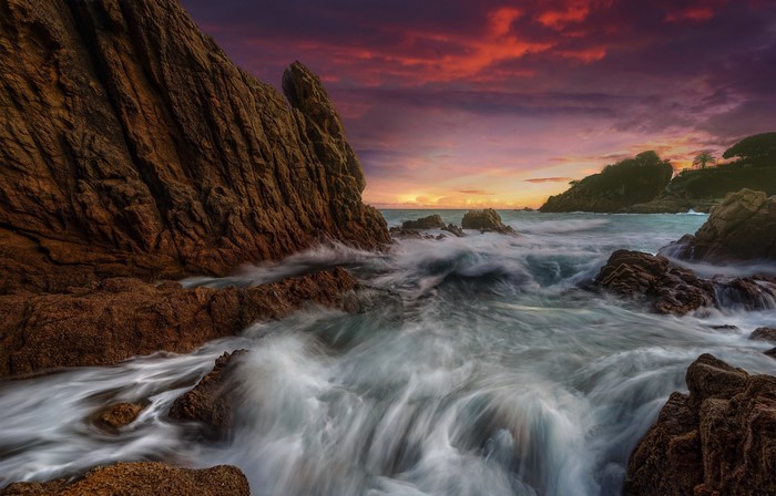 Sunset over rocky coast with waves in Catalonia, Spain