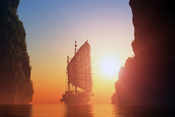 Junk ship sailing between cliffs at sunset