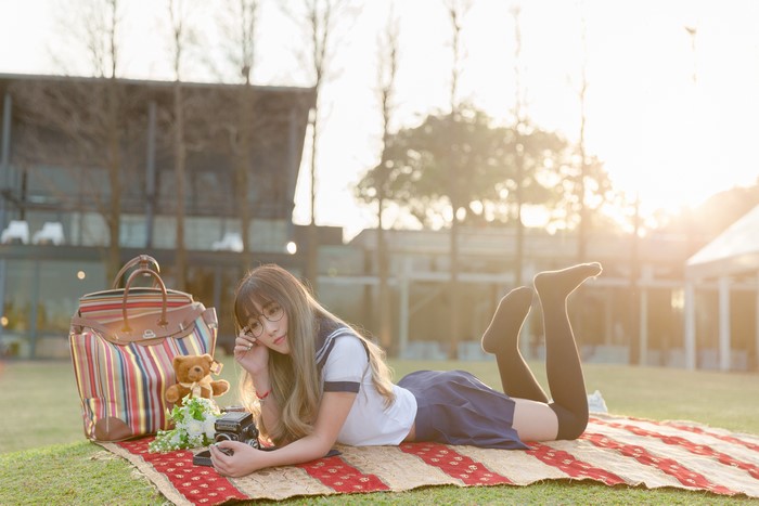Asian schoolgirl with camera and handbag on picnic blanket