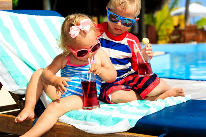 Two children drinking juice by the pool