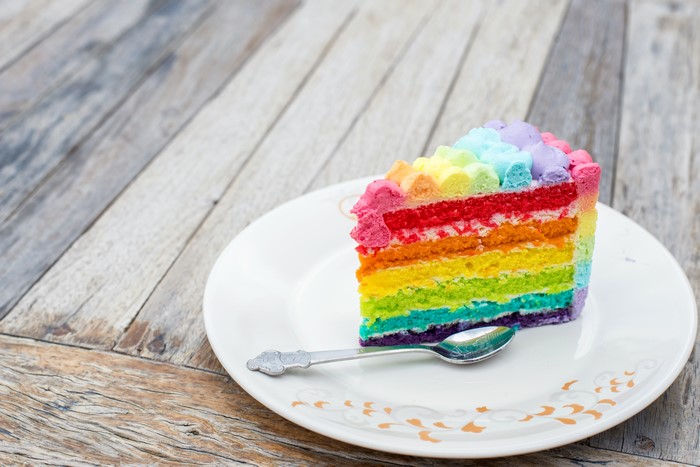Slice of rainbow cake on a plate with a spoon