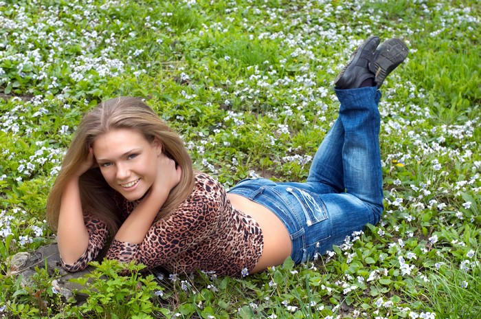 Blonde girl in jeans lying on grass