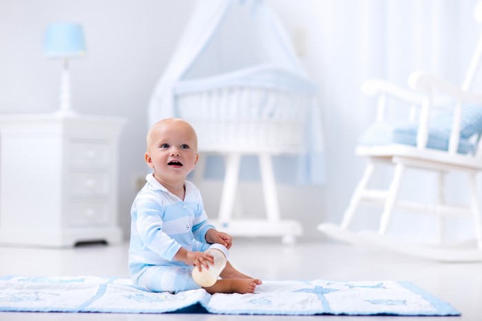 Baby boy sitting with a bottle in a nursery