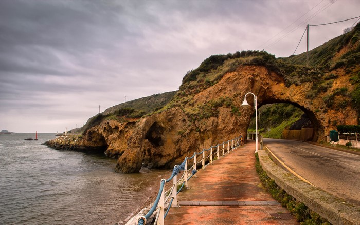 Road through a rock archway on the coast of Aviles Asturias, Spain