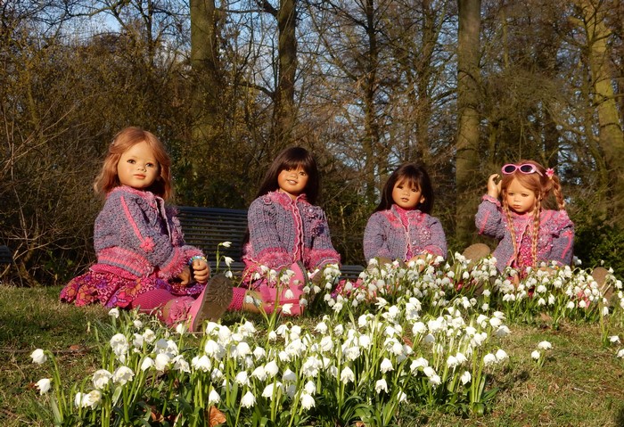 Four dolls sitting in a park with snowdrops