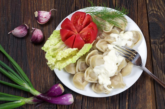 Pelmeni with tomato, lettuce, dill, and sour cream on a plate