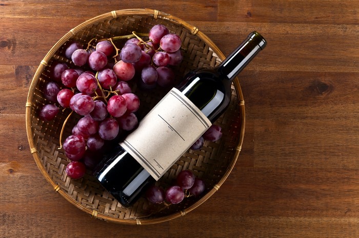 Bottle of Wine and Grapes in Basket on Wood