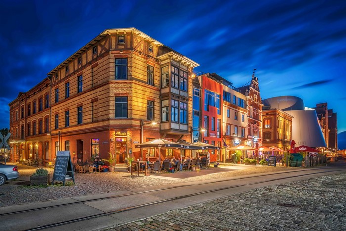 Evening street scene in Stralsund, Germany with illuminated buildings and outdoor seating.